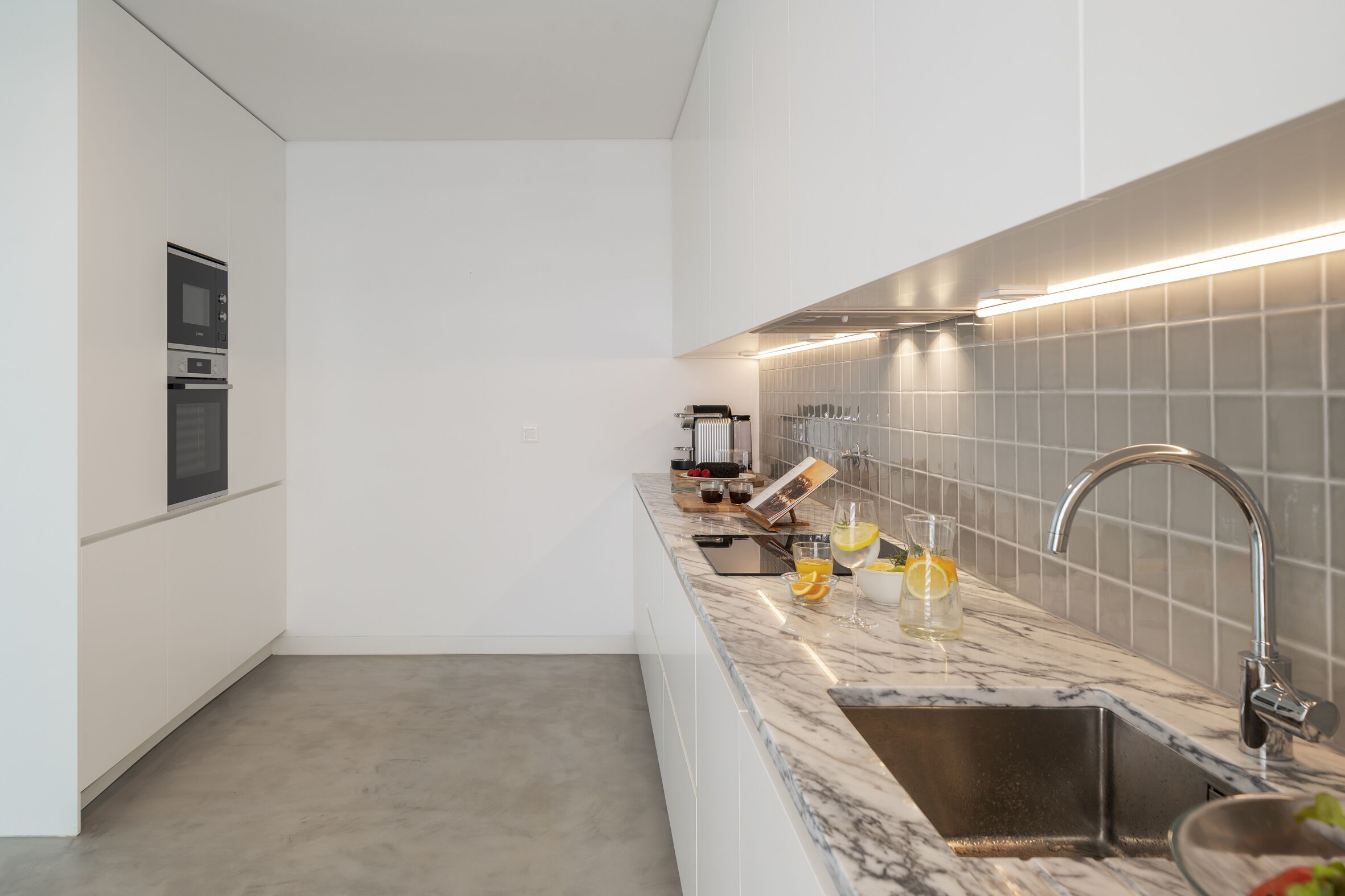 Una cucina moderna con piano di lavoro in marmo, lavello in acciaio inossidabile e forno a incasso.