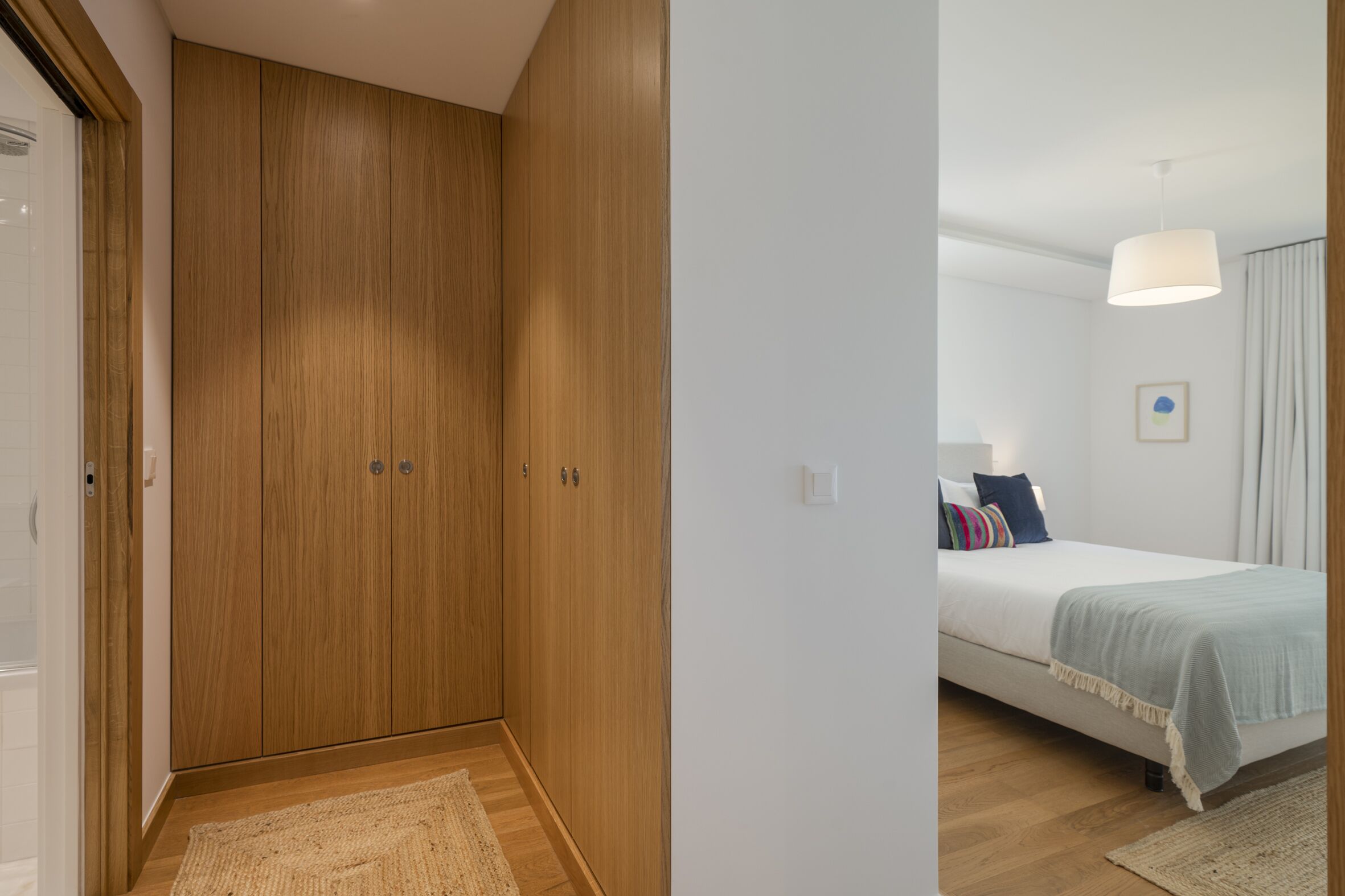 Ein Schlafzimmer mit einem Holzschrank, einem Bett mit blauer und weißer Bettdecke und einer weißen Deckenleuchte.