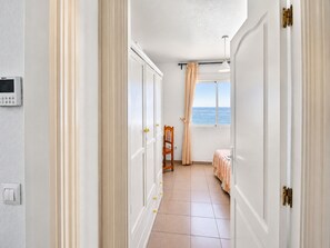 Un couloir donnant sur la mer, une chaise et un lit avec une literie à rayures.