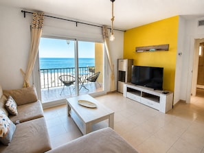 A living room with a sofa, TV, and a balcony with a view of the sea.