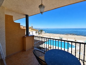 A balcony with a pool, a table, and a chair, overlooking a beach and the sea.