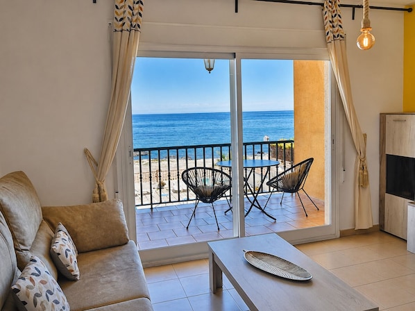 A balcony with a view of the sea, a sofa, two chairs, and a table.