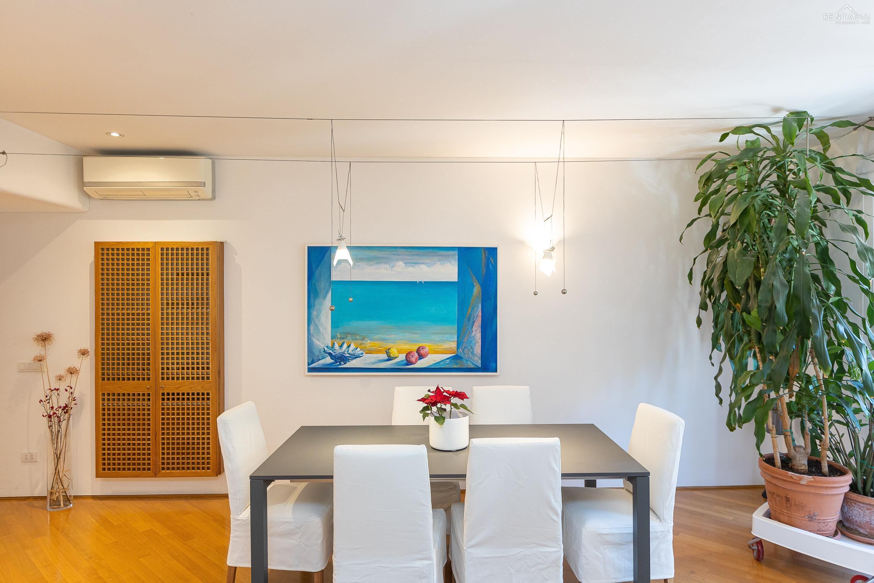 Un coin repas comprenant une table, des chaises, un tableau, un climatiseur et une plante en pot.