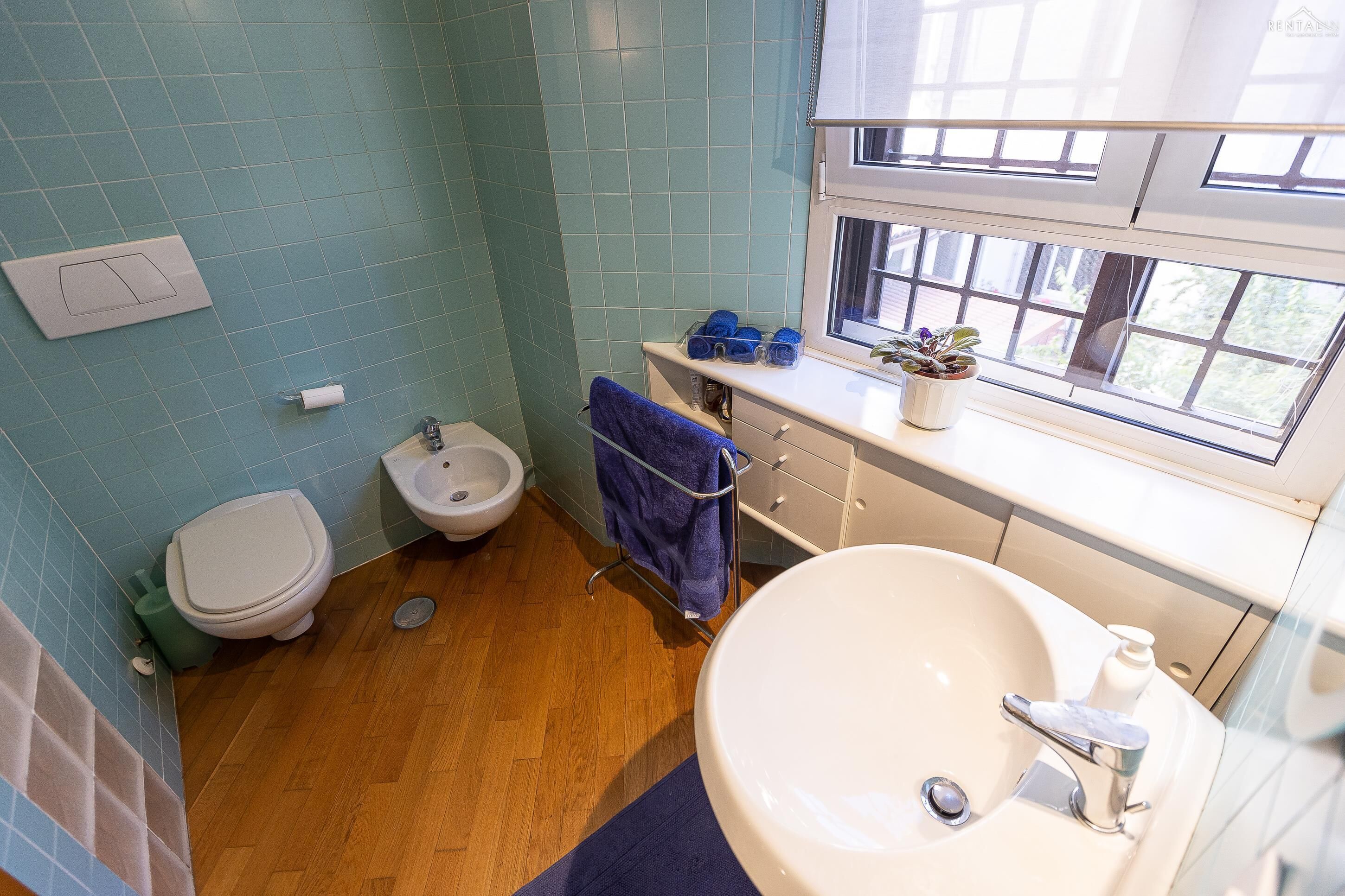 A bathroom with a toilet, bidet, sink, and a window.