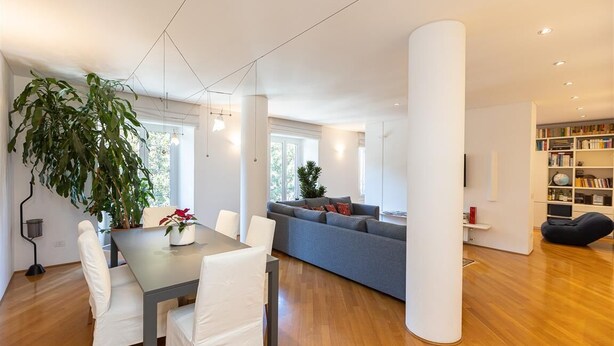 A modern living room with a dining area, a large plant, a grey sofa, and a bookshelf. - San Gioacchino View apartment (Rome)