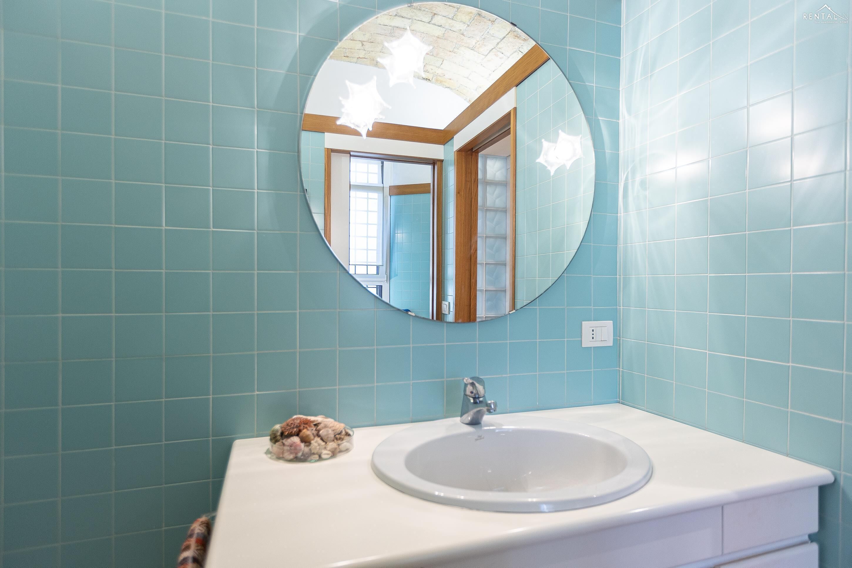 Un bagno con uno specchio rotondo, un lavandino e un piccolo oggetto decorativo sul mobile.