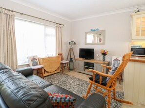 Ein Wohnzimmer mit einer schwarzen Ledersofa, Holzstühlen, einem Fernseher und einer Küchenzeile inklusive Mikrowelle.