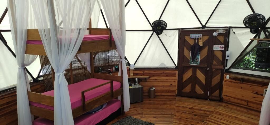 Une tente avec un lit superposé, une porte avec une pancarte et un ventilateur.