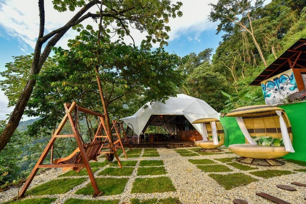 A rustic outdoor seating area with a swing, a covered seating area, and a green wall with a mural.