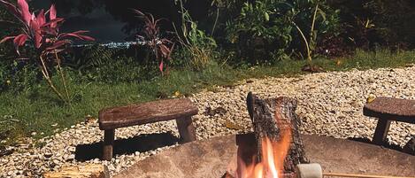 Una fogata con un malvavisco en un palo, rodeada de rocas y plantas.