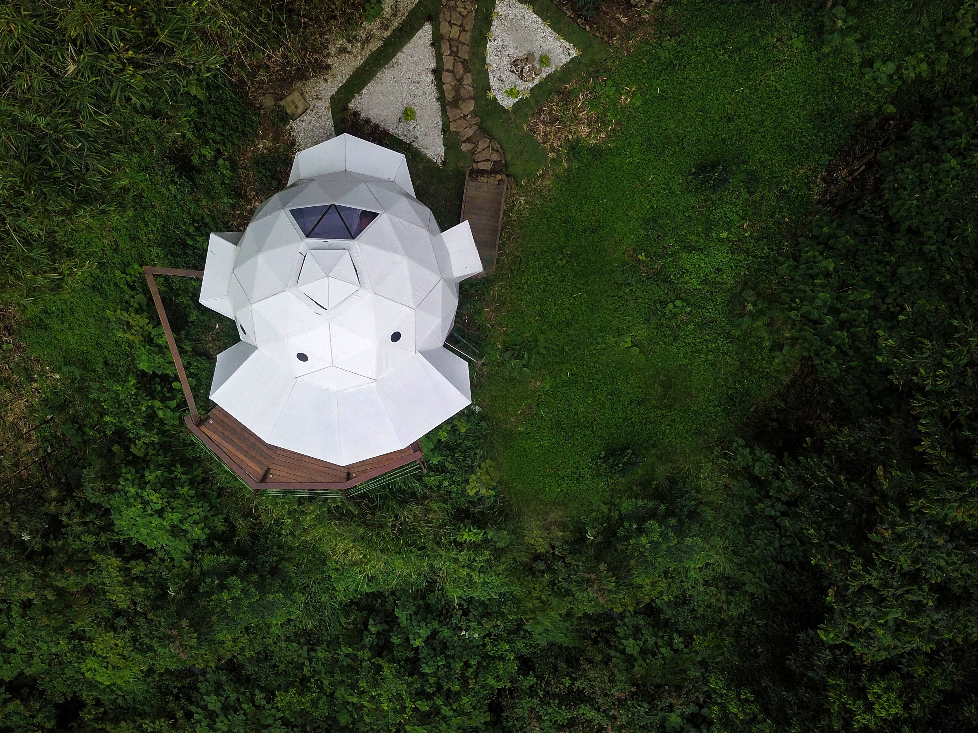 An aerial view of a white, octagonal building with a central skylight, surrounded by dense green foliage.