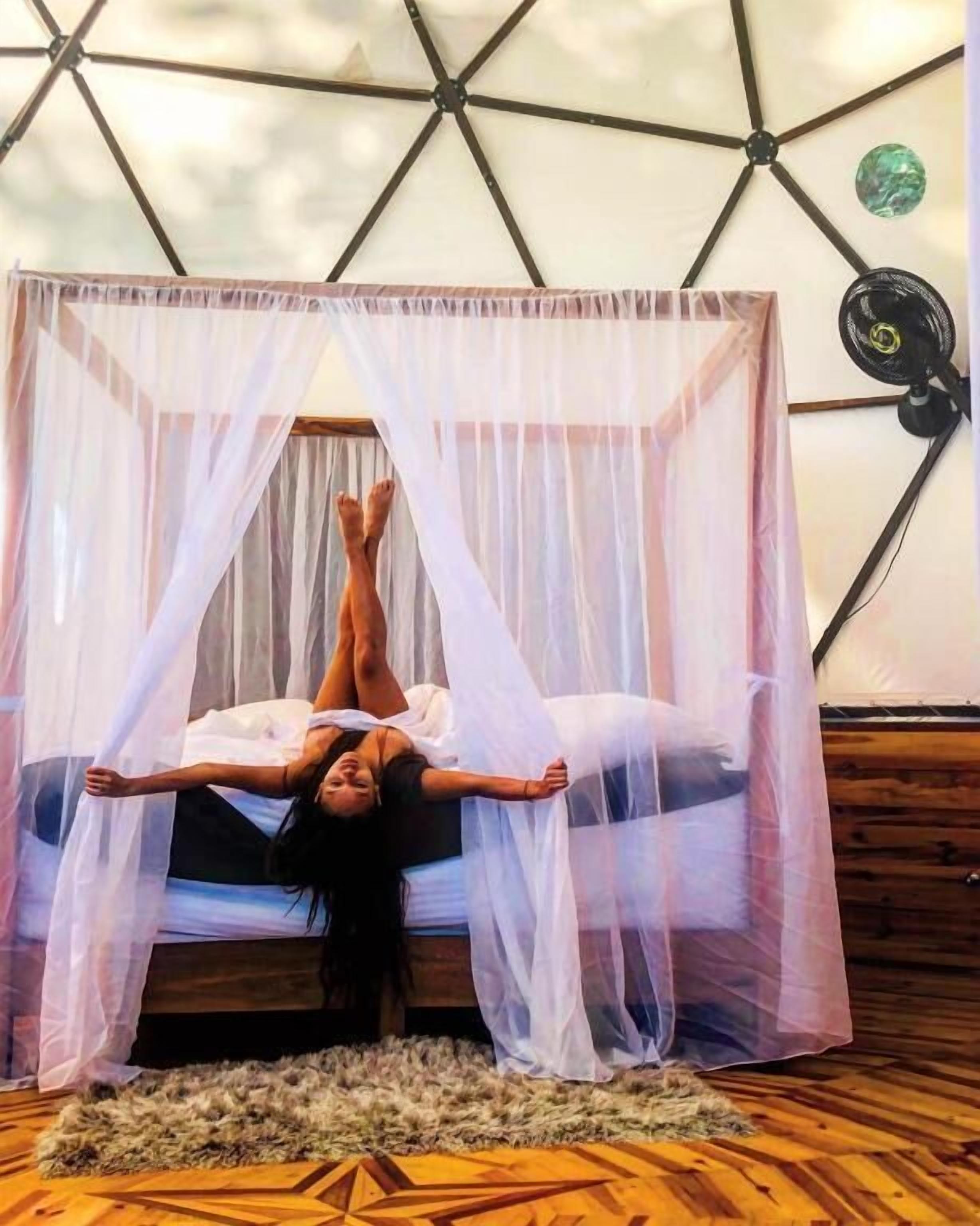 Une chambre avec un lit placé sous un dais transparent, un motif géométrique sur le mur et un plancher en bois.