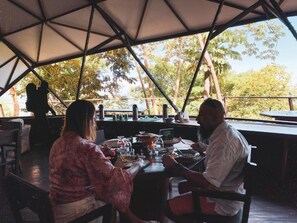 An outdoor dining area with a table set for two, surrounded by a covered structure with a view of trees. - Trekker Glamping (Santa Marta)
