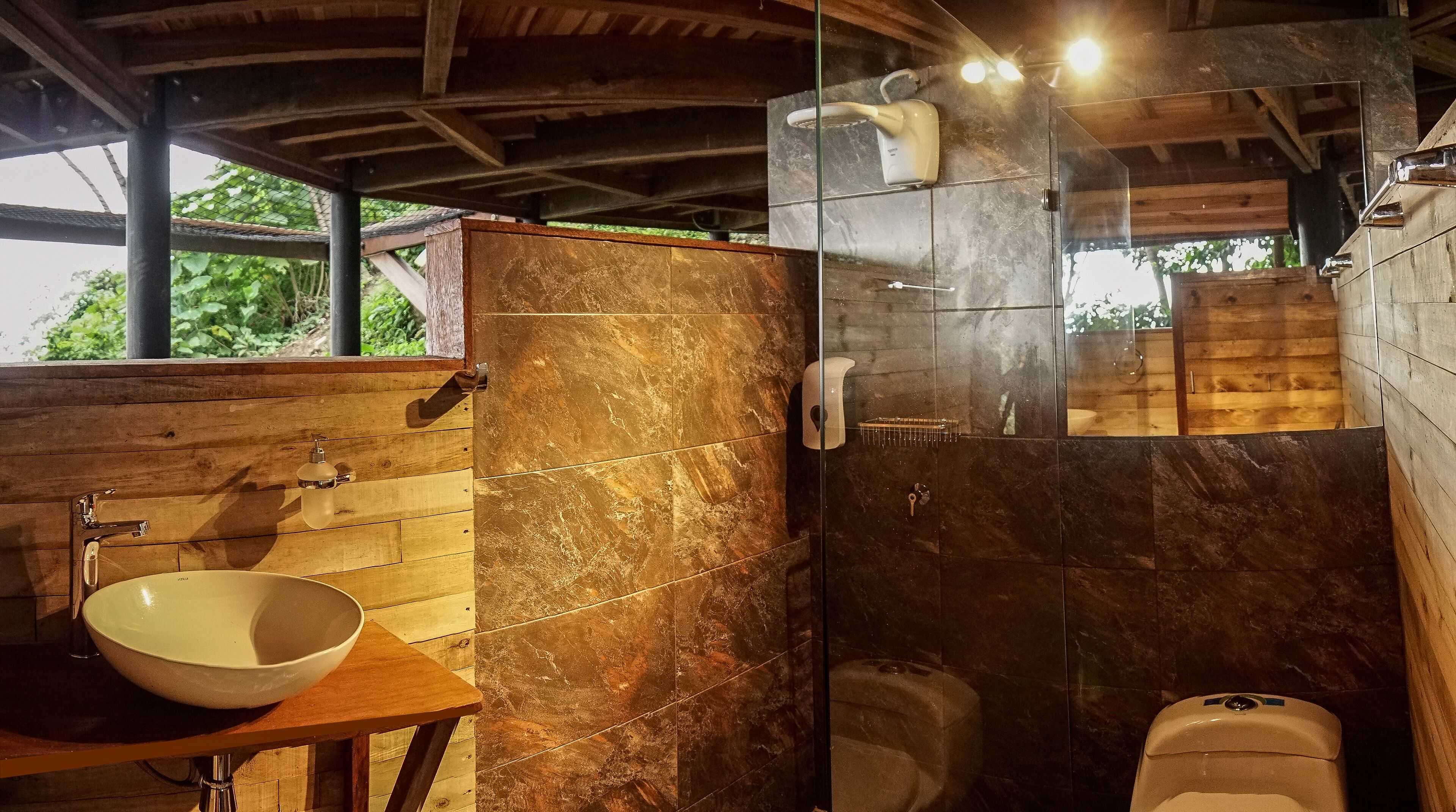A bathroom with a wooden vanity, a bowl sink, a glass shower enclosure, and a toilet.