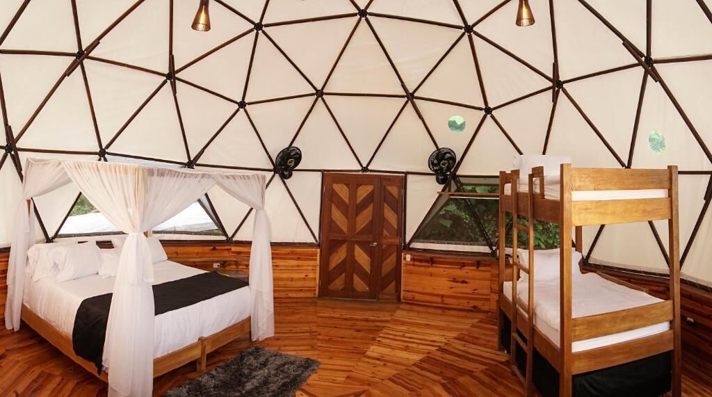 A tent-style room with two wooden beds, a small wooden table, and a geometric-patterned wall.