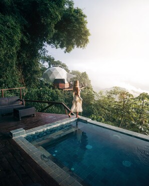 A person standing by a pool with a view of a geodesic dome structure amidst lush greenery. - Trekker Glamping (Santa Marta)