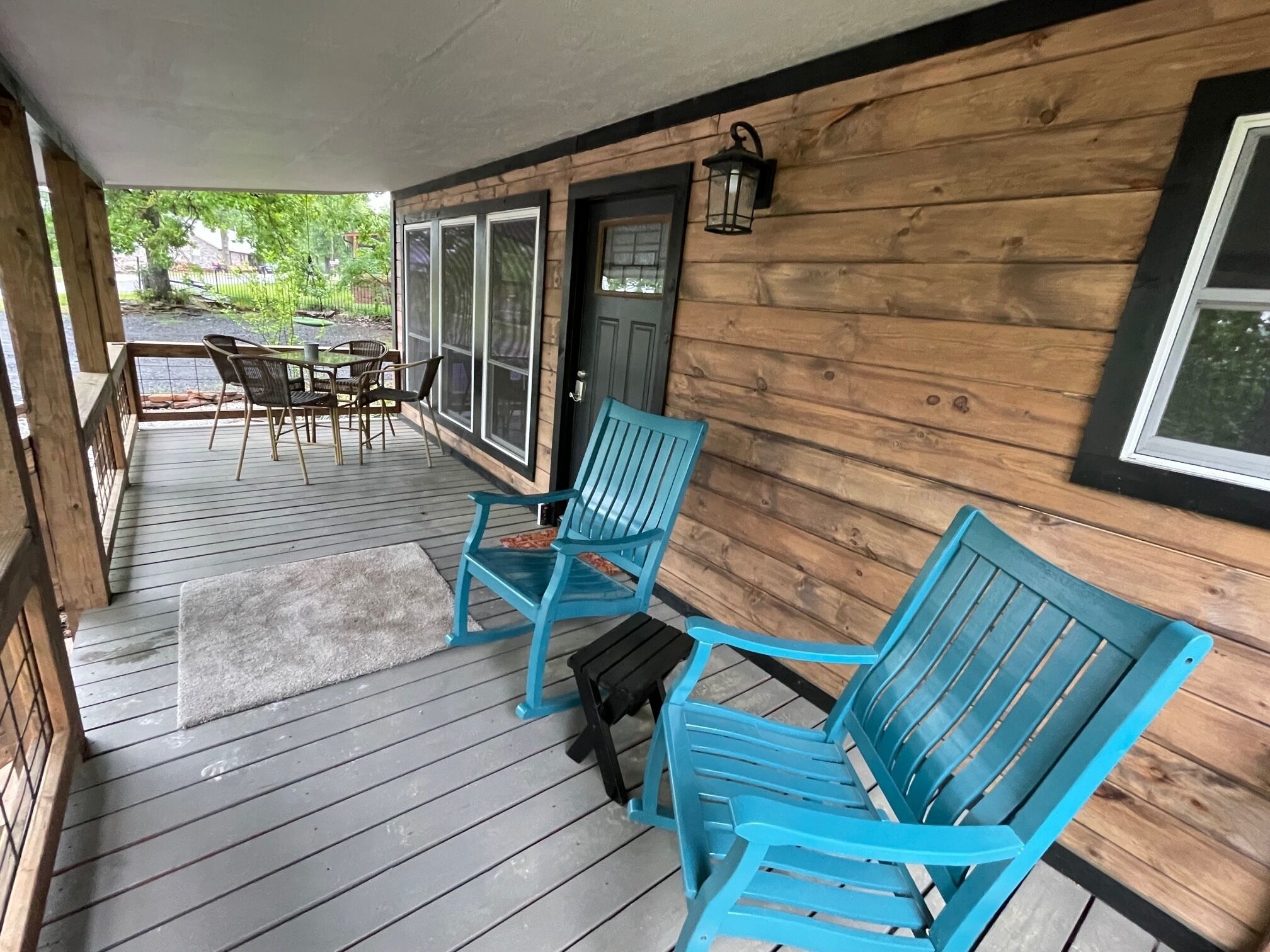 A wooden porch with blue chairs and a table, a door, and a window.