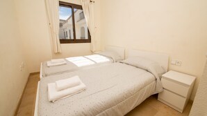 A bedroom with two beds, a window with curtains, a bedside table, and a nightstand. - Marina de la Duquesa 544 (Manilva)
