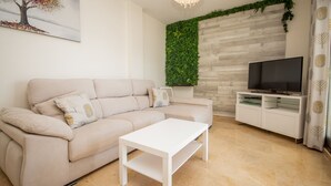 A living room with a beige sofa, a white coffee table, a flat-screen TV on a white cabinet, and a green vertical garden wall. - Marina de la Duquesa 544 (Manilva)