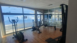 Une salle de sport équipée de machines de cardio, d’un rameur et offrant une vue sur un paysage enneigé grâce à de grandes fenêtres.