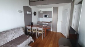 Un espace de vie compact comprenant un canapé, une table à manger, des chaises, un coin cuisine avec un four à micro-ondes et une chambre en mezzanine avec balcon.