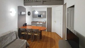 Un espace de vie compact comprenant un coin repas, une kitchenette et une chambre en mezzanine.