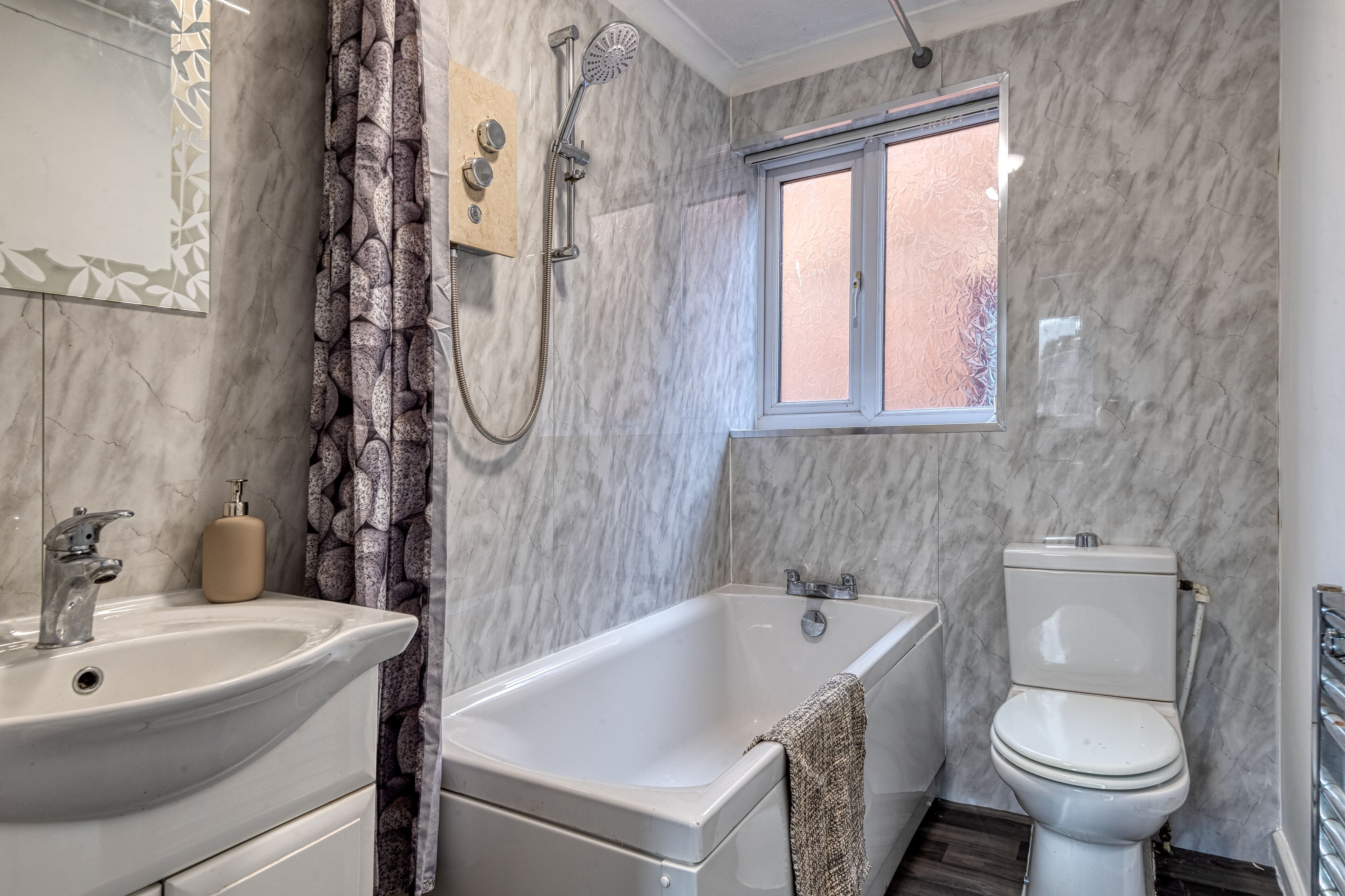 Un baño con pared de mármol, una bañera, un inodoro y un lavamanos.