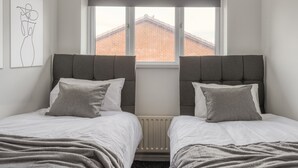 A bedroom with two beds, a window with a view of a brick building, and a radiator below the window.