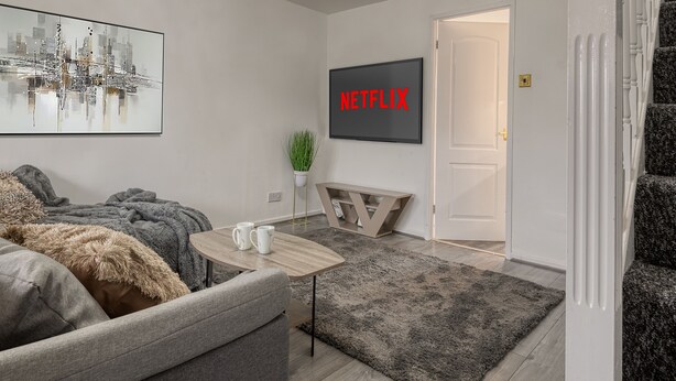 A modern living room with a grey sofa, a coffee table, a framed cityscape picture, a Netflix sign, and a staircase.