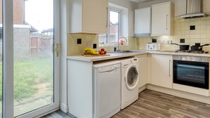 A compact kitchen with a washing machine, oven, and a window overlooking a backyard.