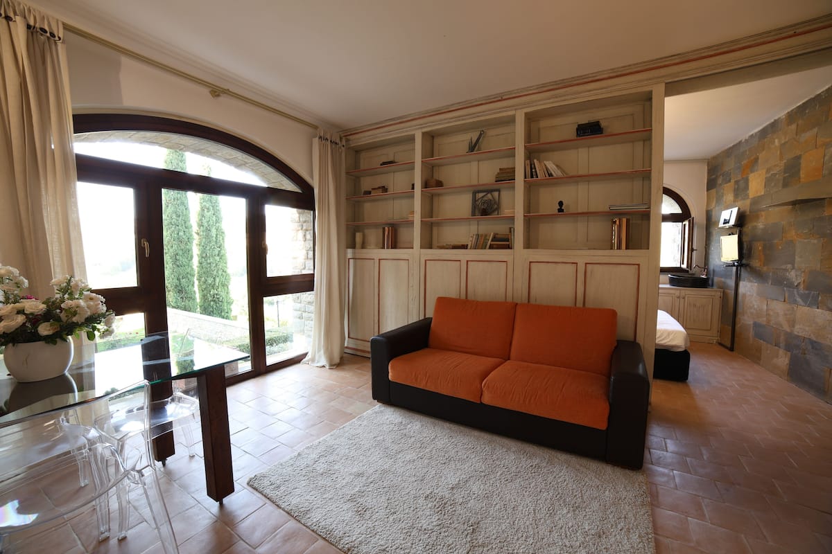 A living room with a glass coffee table, a sofa, a bookshelf, and a stone wall.