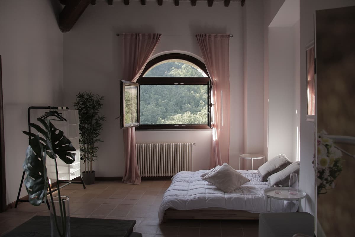 A bedroom with a bed, bedside table, window, radiator, curtains, and a potted plant.
