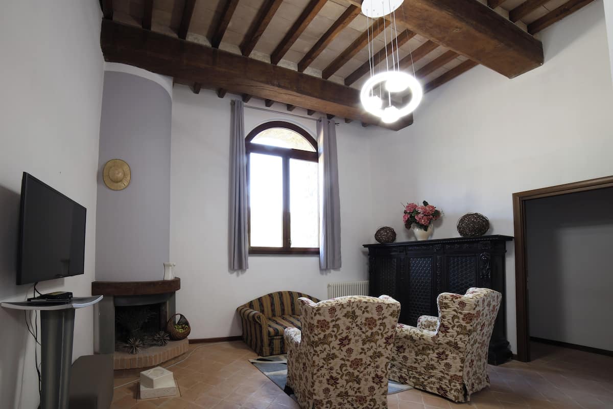 A living room with a fireplace, two armchairs, a television, and a ceiling fan.