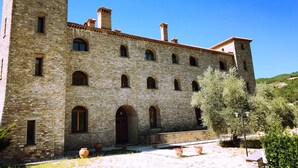 A stone building with multiple arched windows and a courtyard with potted plants. - HT CASTELLO DI CAMPOLONGO (Valfabbrica)