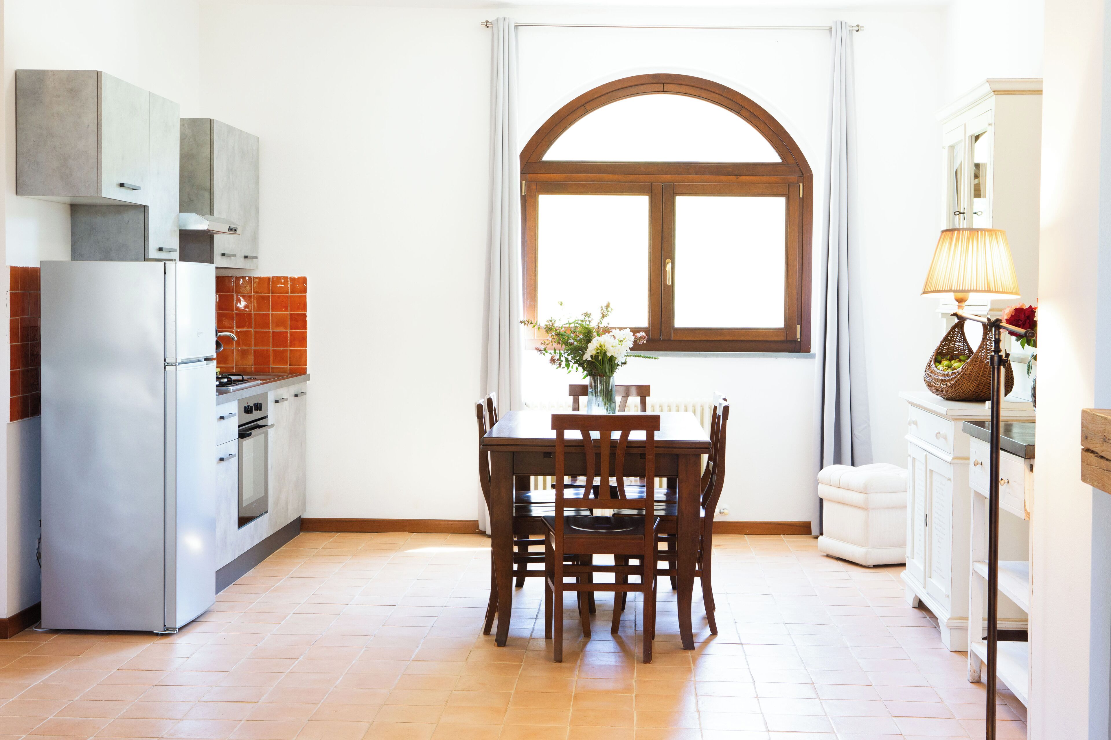 A kitchen with a dining table, chairs, a refrigerator, cabinets, and a window with curtains.