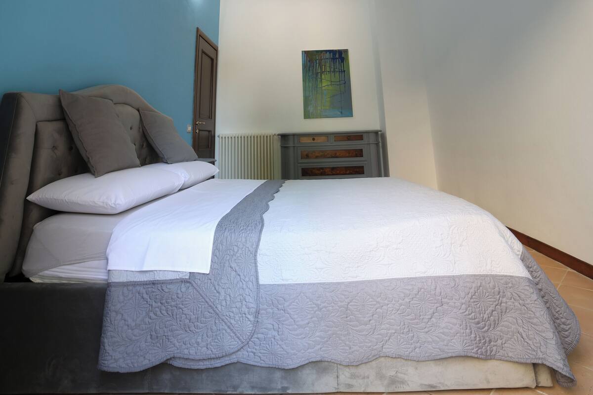 A bedroom with a bed, pillows, a radiator, and a painting on the wall.
