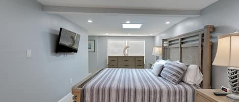 A bedroom with a bed, bedside table, lamp, and a mounted TV.
