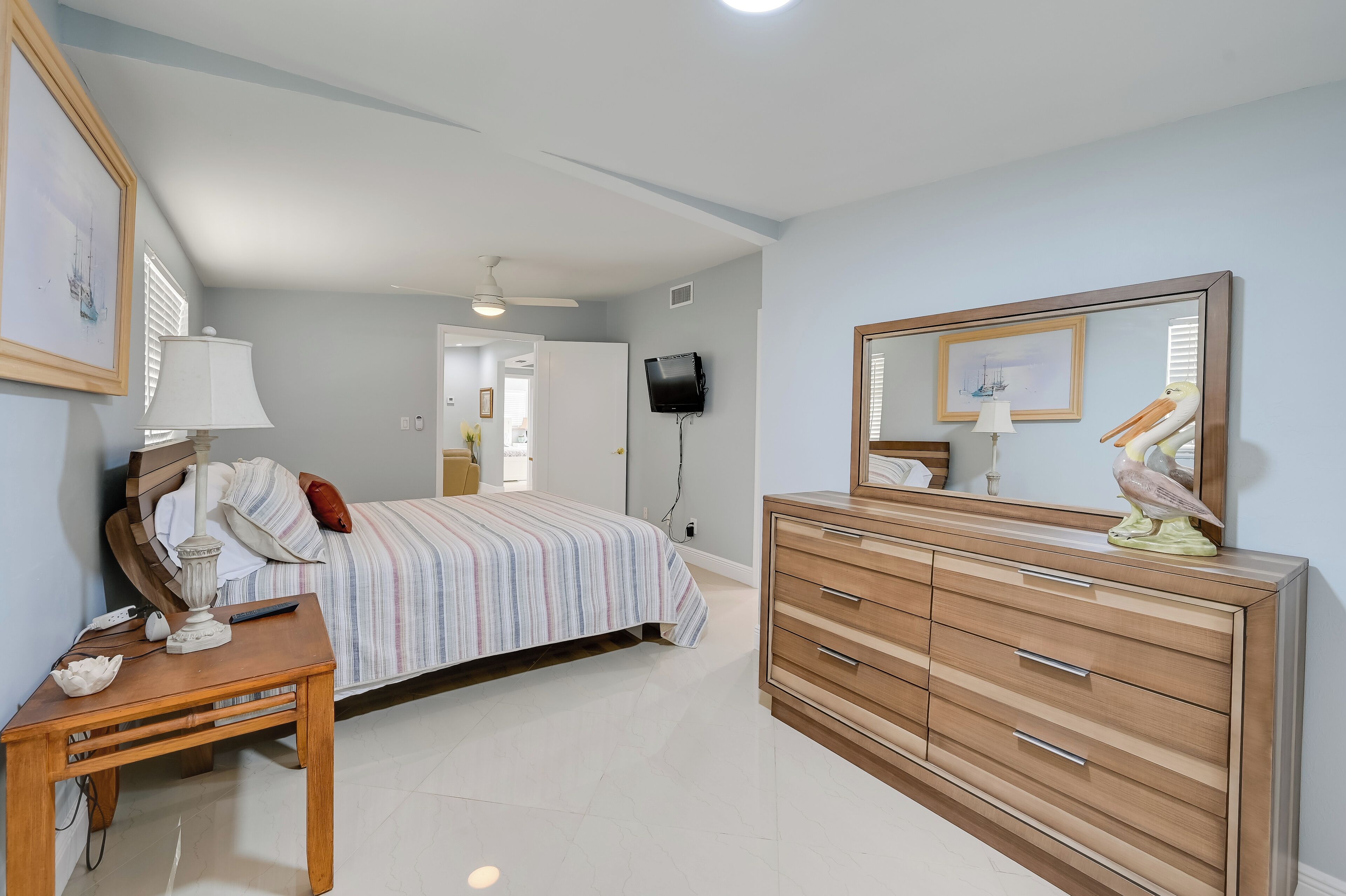 Une chambre à coucher comprenant un lit, une table de chevet, une commode et un téléviseur fixé au mur.