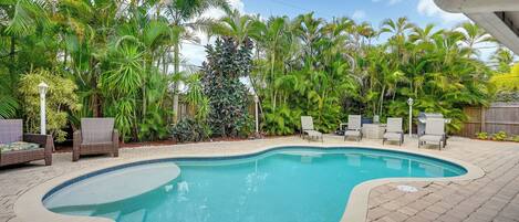 A swimming pool with a curved edge, surrounded by a brick patio and various plants.