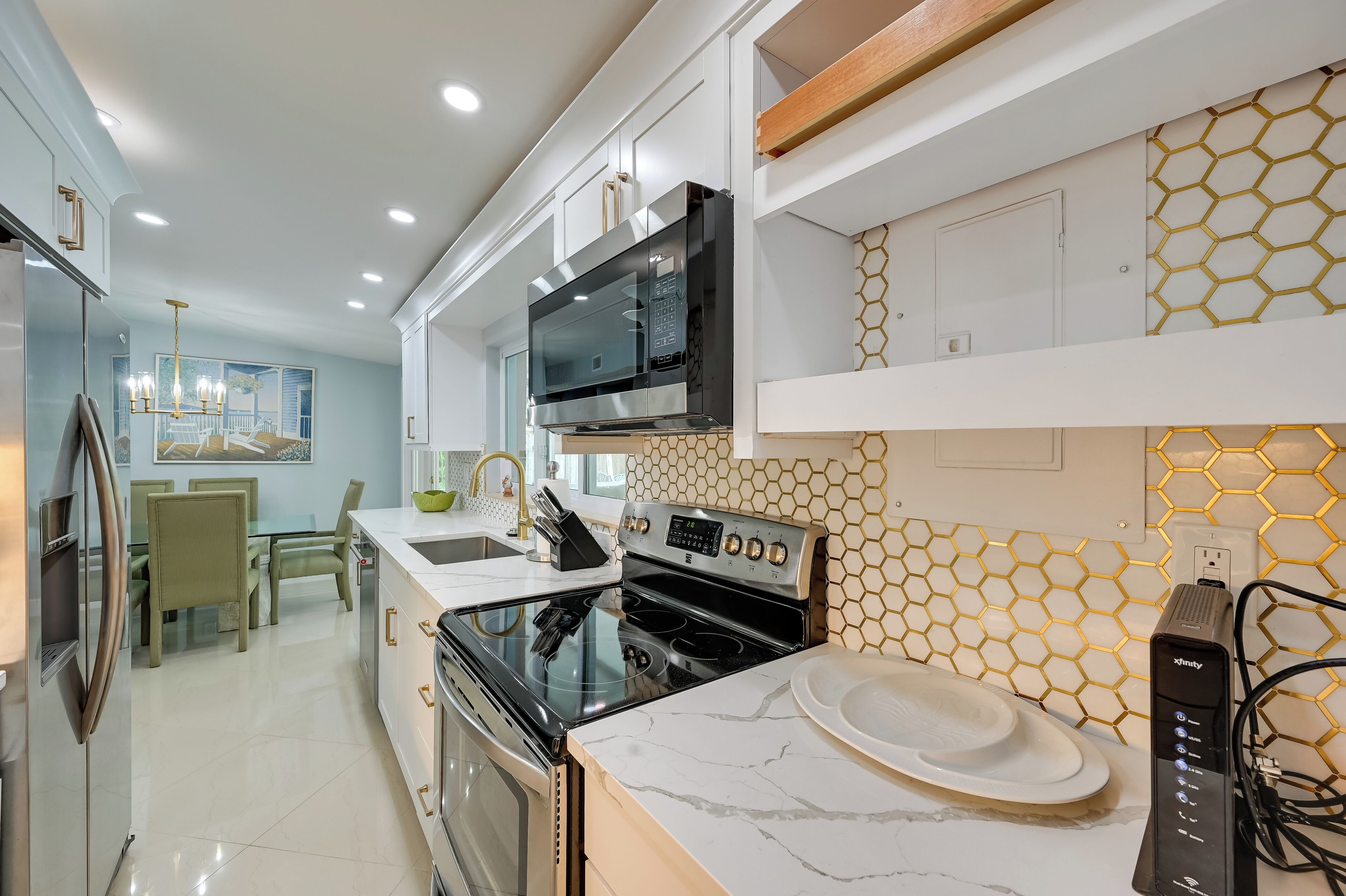 A modern kitchen with white cabinetry, a black microwave, stainless steel appliances, and a hexagonal tile backsplash.