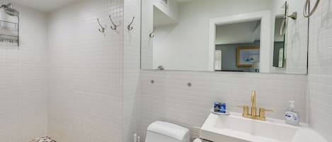 Een badkamer met witte betegelde wanden, een douche, toilet en een wastafel met gouden kraan, en een spiegel.