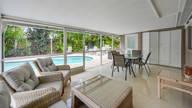 A modern indoor space with a glass wall overlooking a swimming pool, wicker furniture, and a dining area. - Pelican Nest, Tropical Naples Villa w/ Pool (Naples)