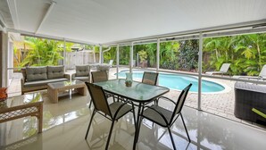 A spacious patio with a glass table and chairs, a sofa, and a pool view. - Pelican Nest, Tropical Naples Villa w/ Pool (Naples)