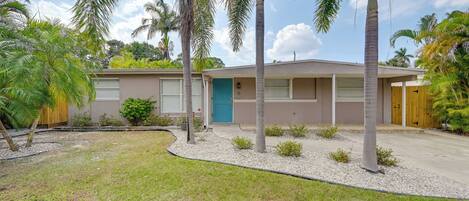 A single-story house with a front garage, a blue door, and a small front yard with palm trees and a gravel pathway.