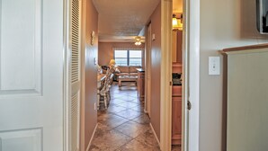A hallway leading to a dining area with a ceiling fan, a window with blinds, and a kitchen area with cabinets and a countertop. - Beachfront St Petersburg Condo w/ Community Pool! (Treasure Island)