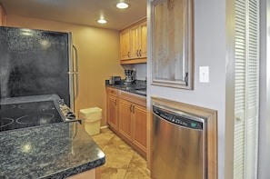 A kitchen with a stainless steel refrigerator, a dishwasher, wooden cabinets, and a granite countertop.