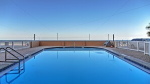 A rectangular swimming pool with a metal ladder on the left, surrounded by a white fence and a brick wall. - Beachfront St Petersburg Condo w/ Community Pool! (Treasure Island)