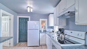 A modern kitchen with white appliances, a stainless steel kettle, and a marble countertop.
