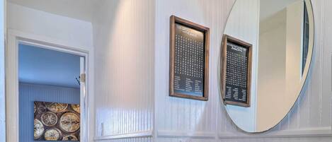 A bathroom with a sink, mirror, and toilet paper holder. There is a door leading to a dining area with a table and chairs.