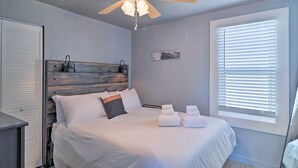 A bedroom with a bed, a ceiling fan, a window with blinds, and a door.